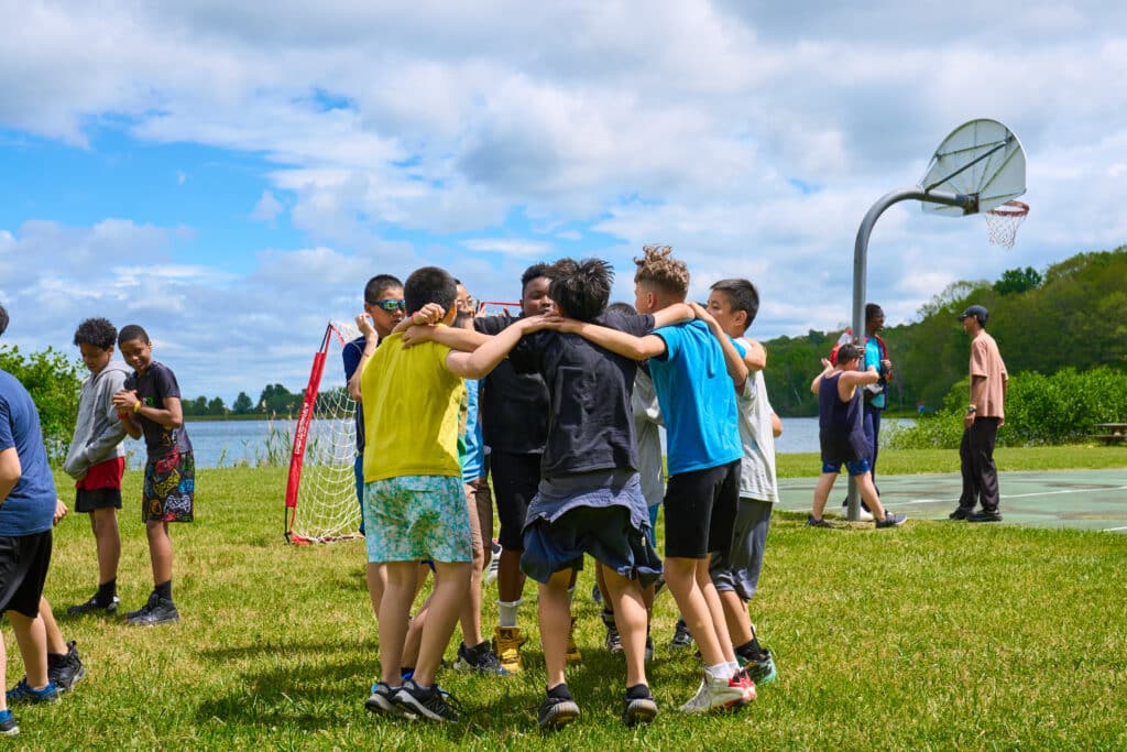 Campers, Alfred and Jayden, huddle with friends on the ballfield overlooking the camp lake.