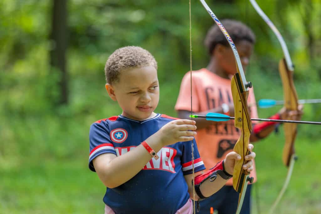 Ethan, a camper at Camp Hidden Valley, learns how to aim arrows in archery.